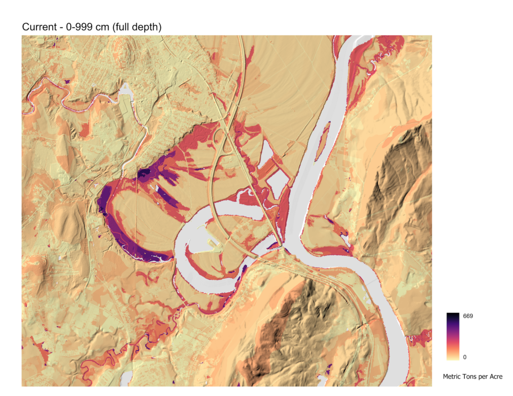Map showing estimated current soil organic carbon storage at full soil depth across a river valley landscape in Massachusetts. Wetlands along river corridors appear in deep red and purple, indicating the highest carbon density. Upland areas appear in pale tan, indicating lower storage.